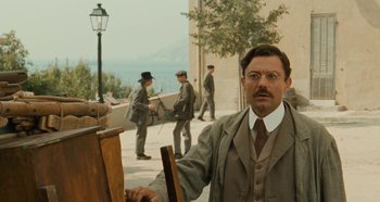 Movie still from “My Father's Glory” (1990), directed by Yves Robert – A man in a suit and tie standing in front of a wooden easel; Medium shot, Low angle