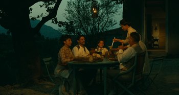 Movie still from “My Father's Glory” (1990), directed by Yves Robert – A group of people sitting around a table at night; Wide shot, High angle