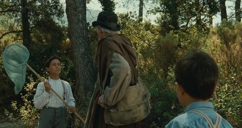 Movie still from “My Father's Glory” (1990), directed by Yves Robert – An old man wearing a hat is holding a bag; Medium shot, Over the shoulder angle