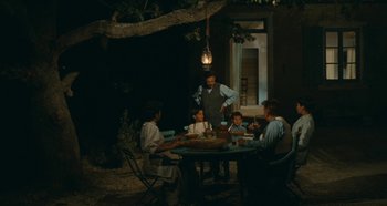 Movie still from “My Father's Glory” (1990), directed by Yves Robert – A group of people sitting around a table at night; Wide shot, High angle