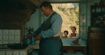 Movie still from “My Father's Glory” (1990), directed by Yves Robert – A man in an apron is in a kitchen with two children; Medium shot, Over the shoulder angle