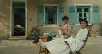 Movie still from “My Father's Glory” (1990), directed by Yves Robert – A woman sitting on a chair in front of a house; Wide shot, High angle
