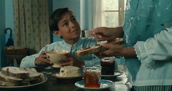 Movie still from “My Father's Glory” (1990), directed by Yves Robert – A young boy sitting at a table with a sandwich; Medium shot, Over the shoulder angle