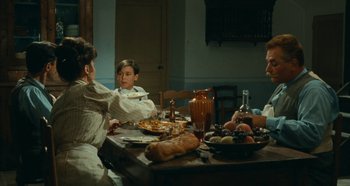 Movie still from “My Father's Glory” (1990), directed by Yves Robert – Three people sitting at a dinner table eating pizza; Medium shot, High angle