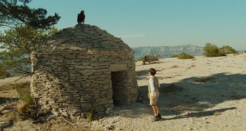 Movie still from “My Father's Glory” (1990), directed by Yves Robert – A man standing in front of a stone building; Extreme Wide shot, Low angle