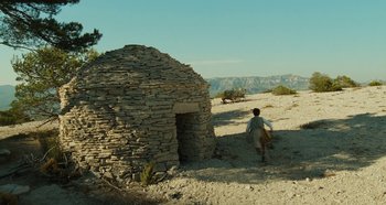 Movie still from “My Father's Glory” (1990), directed by Yves Robert – A person walking in front of an old stone building; Extreme Wide shot, Low angle