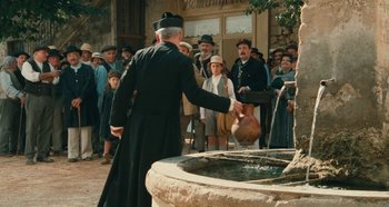 Movie still from “My Father's Glory” (1990), directed by Yves Robert – An old man in a priest's outfit is by a fountain; Wide shot, High angle