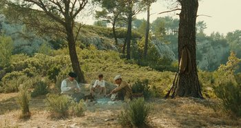 Movie still from “My Father's Glory” (1990), directed by Yves Robert – A group of men sitting around a fire in the woods; Wide shot, High angle
