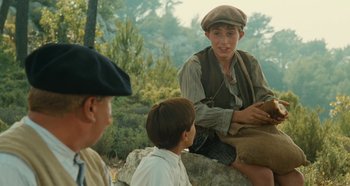 Movie still from “My Father's Glory” (1990), directed by Yves Robert – A group of people sitting on top of a rock in a field; Medium shot, Over the shoulder angle