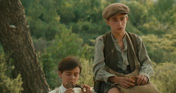 Movie still from “My Father's Glory” (1990), directed by Yves Robert – Two young boys sitting on the ground eating some food; Medium shot, High angle