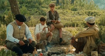 Movie still from “My Father's Glory” (1990), directed by Yves Robert – A group of people sitting on a rock near a campfire; Wide shot, High angle