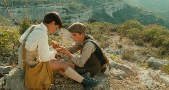 Movie still from “My Father's Glory” (1990), directed by Yves Robert – Two young boys sitting on the ground eating food; Medium shot, High angle