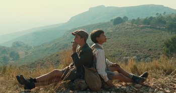 Movie still from “My Father's Glory” (1990), directed by Yves Robert – Two young men sitting on a rock in the mountains; Medium shot, Low angle