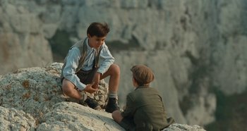 Movie still from “My Father's Glory” (1990), directed by Yves Robert – Two young men sitting on a rock face; Medium shot, High angle