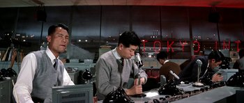 Movie still from “My Geisha” (1962), directed by Jack Cardiff – A man sitting in front of a microphone in an office; Medium shot, Low angle