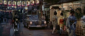 Movie still from “My Geisha” (1962), directed by Jack Cardiff – An old car parked on the side of the street; Wide shot, Low angle