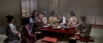 Movie still from “My Geisha” (1962), directed by Jack Cardiff – A group of people sitting around a table eating food; Wide shot, High angle
