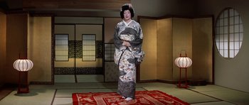 Movie still from “My Geisha” (1962), directed by Jack Cardiff – A geisha standing on a red rug in a room; Wide shot, Low angle