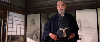 Movie still from “My Geisha” (1962), directed by Jack Cardiff – An older man in a kimono standing in front of a painting; Medium shot, Low angle
