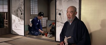Movie still from “My Geisha” (1962), directed by Jack Cardiff – A man with a beard is sitting in front of a painting; Medium shot, Over the shoulder angle