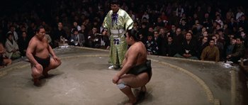 Movie still from “My Geisha” (1962), directed by Jack Cardiff – A sumo wrestler kneeling down in front of a crowd of people; Wide shot, High angle