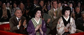 Movie still from “My Geisha” (1962), directed by Jack Cardiff – A woman in a purple kimono clapping in front of a group of people; Medium shot, Low angle