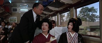 Movie still from “My Geisha” (1962), directed by Jack Cardiff – Two women and a man on a train; Medium shot, Low angle