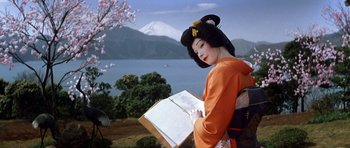 Movie still from “My Geisha” (1962), directed by Jack Cardiff – A geisha reading a book near a body of water; Medium shot, Low angle