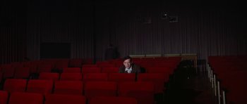 Movie still from “My Geisha” (1962), directed by Jack Cardiff – A man sitting in an empty theater with red seats; Wide shot, High angle