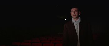 Movie still from “My Geisha” (1962), directed by Jack Cardiff – A man standing in front of an audience in a dark room; Medium shot, Low angle
