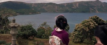 Movie still from “My Geisha” (1962), directed by Jack Cardiff – A woman in a purple top holding an umbrella in front of a body of water; Extreme Wide shot, High angle