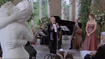 Movie still from “My Left Foot” (1989), directed by Jim Sheridan – An older man holding a microphone while a group of people play music; Wide shot, Over the shoulder angle