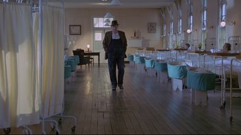 Movie still from “My Left Foot” (1989), directed by Jim Sheridan – A man walking in a room with chairs around him; Wide shot, Low angle