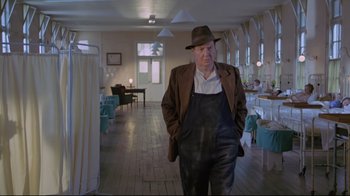 Movie still from “My Left Foot” (1989), directed by Jim Sheridan – An older man wearing a hat and overalls in a room; Medium shot, Low angle