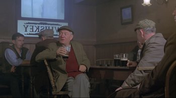Movie still from “My Left Foot” (1989), directed by Jim Sheridan – An older man sitting in a chair holding a drink; Medium shot, High angle