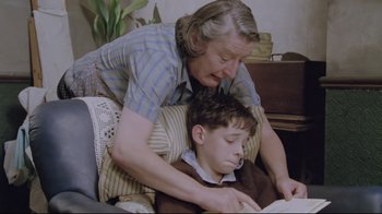 Movie still from “My Left Foot” (1989), directed by Jim Sheridan – An older woman helping a young boy read a book; Medium shot, High angle