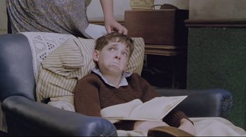 Movie still from “My Left Foot” (1989), directed by Jim Sheridan – A boy is sitting in a chair reading a book; Medium shot, High angle