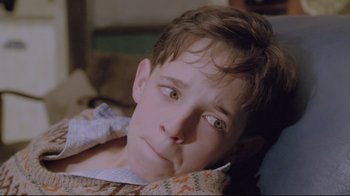 Movie still from “My Left Foot” (1989), directed by Jim Sheridan – A young boy with green eyes laying in a bed; Close Up shot, High angle