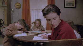 Movie still from “My Left Foot” (1989), directed by Jim Sheridan – A woman writing on a piece of paper while sitting at a table with two other children; Medium shot, Low angle