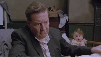 Movie still from “My Left Foot” (1989), directed by Jim Sheridan – An older man in a suit is holding a baby; Close Up shot, Over the shoulder angle