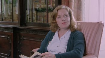 Movie still from “My Left Foot” (1989), directed by Jim Sheridan – A woman sitting in a chair holding a book; Medium shot, Over the shoulder angle