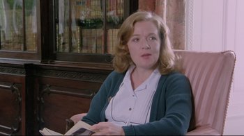 Movie still from “My Left Foot” (1989), directed by Jim Sheridan – A woman sitting in a chair holding an open book; Medium shot, Over the shoulder angle