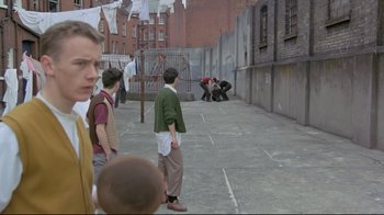 Movie still from “My Left Foot” (1989), directed by Jim Sheridan – A group of people standing on the side of the street; Wide shot, Over the shoulder angle