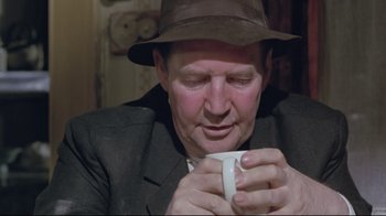 Movie still from “My Left Foot” (1989), directed by Jim Sheridan – A man in a hat is holding a coffee cup; Close Up shot, Over the shoulder angle
