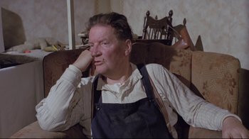 Movie still from “My Left Foot” (1989), directed by Jim Sheridan – An older man sitting in a chair with his hand on his face; Medium shot, High angle