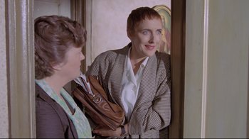 Movie still from “My Left Foot” (1989), directed by Jim Sheridan – A woman holding a brown purse in front of another woman; Medium shot, Over the shoulder angle
