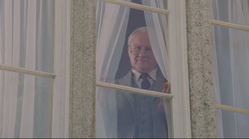 Movie still from “My Left Foot” (1989), directed by Jim Sheridan – An older man looking out a window with white curtains; Medium shot, Low angle
