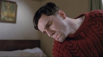 Movie still from “My Left Foot” (1989), directed by Jim Sheridan – A man in a red sweater with his eyes closed; Close Up shot, Low angle