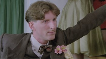 Movie still from “My Left Foot” (1989), directed by Jim Sheridan – A man in a suit and bow tie with a flower in his hair; Close Up shot, Low angle