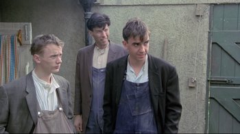 Movie still from “My Left Foot” (1989), directed by Jim Sheridan – A group of men standing next to each other in front of a building; Medium shot, Low angle